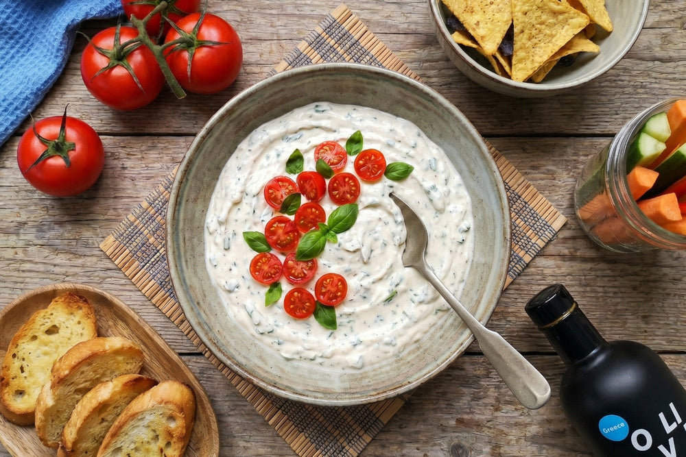 Eine cremige Bruschetta Sauce ist mit Tomaten und Basilikum garniert, daneben liegen geröstetes Brot, Gemüse und Tortilla-Chips