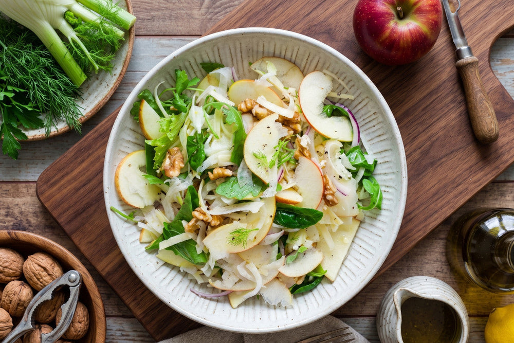 Ein Apfel-Fenchel-Salat mit Walnüssen, Käse, Rucola und feinen Apfelscheiben liegt in einer hellen Schale