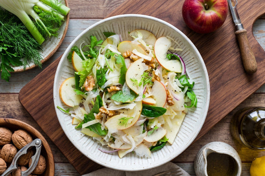 Ein Apfel-Fenchel-Salat mit Walnüssen, Käse, Rucola und feinen Apfelscheiben liegt in einer hellen Schale