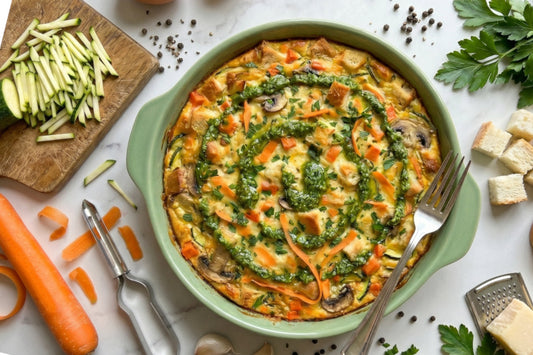 Eine goldgelbe Eier-Frittata mit Gemüse, Parmesan, Kräutern, Rüebli und Zucchetti liegt in einer grünen Ofenform