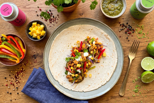 Eine Tortilla ist mit würzigem Poulet, Peperoni, Mango und Kräutern belegt; daneben stehen Salsa Verde und Gewürzdosen
