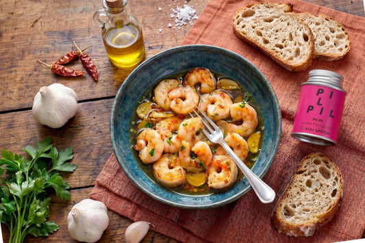 Gambas Pil-Pil liegen in Olivenöl mit Knoblauch, Chili und Petersilie; daneben stehen Brot, Gewürzdose und Olivenö