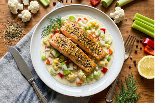Zwei Lachsfilets liegen auf cremigem Gemüse an Cointreau-Sauce, daneben sind Dill, Zitrone und frisches Gemüse zu sehen