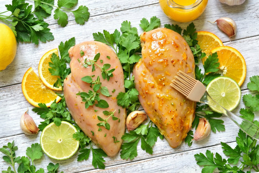 Zwei Pouletbrüste liegen mit kubanischer Mojo Marinade, Orangen, Limetten, Kräutern und Knoblauch auf hellem Holz