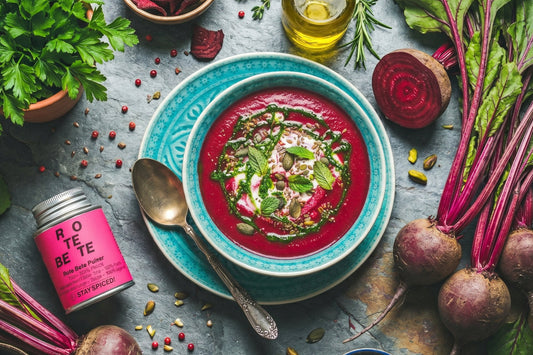 Eine rubinrote Randen Suppe steht mit Kokos-Minze Rahmschaum, Kürbiskernen, Pistazien und frischen Randen auf dem Tisch