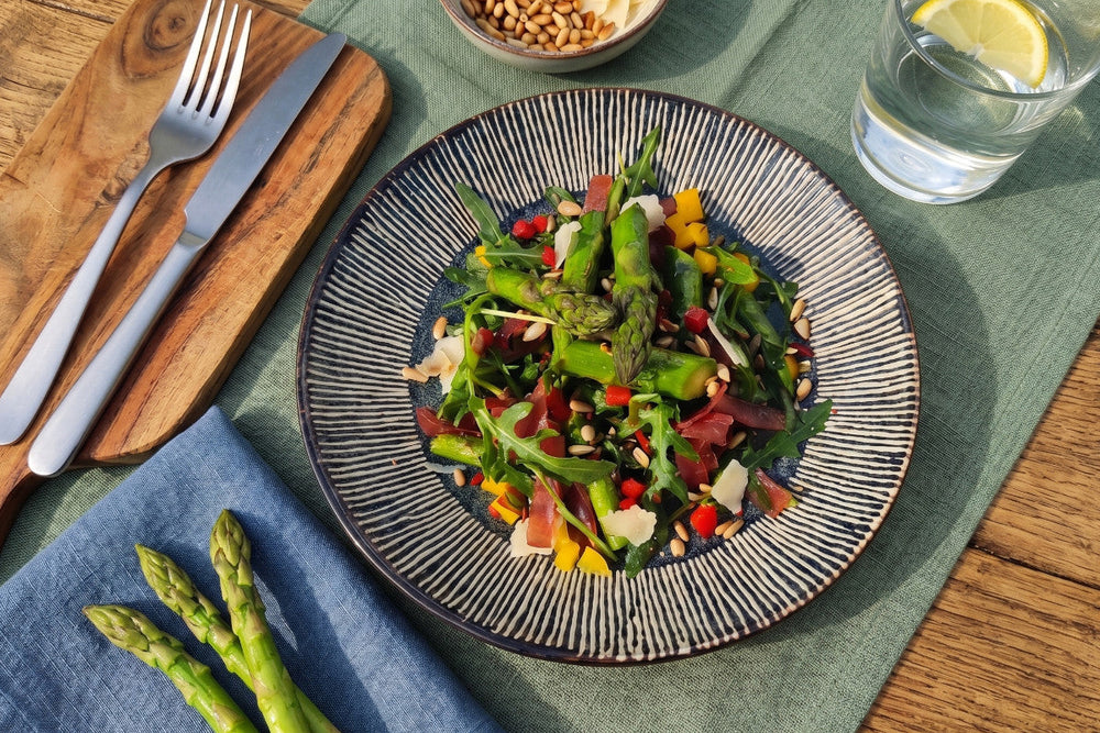 Ein Spargel-Salat mit Rucola, Bündnerfleisch, Peperoni, Pinienkernen und Parmesan liegt auf einem Teller