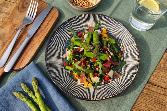 Ein Spargel-Salat mit Rucola, Bündnerfleisch, Peperoni, Pinienkernen und Parmesan liegt auf einem Teller