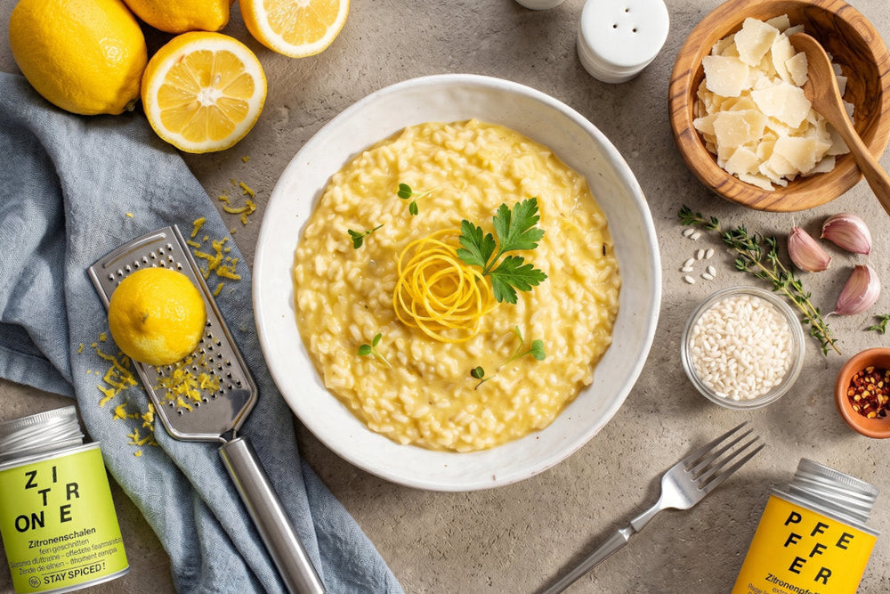 Ein cremiges Zitronen-Risotto steht mit Zitronenzeste, Parmesan, Risottoreis, Knoblauch und frischen Zitronen auf dem Tisch