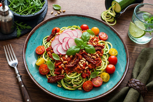 Zucchini-Spaghetti mit rotem Pesto liegen auf einem Teller, garniert mit Tomaten, Radieschen, Basilikum und Pinienkernen
